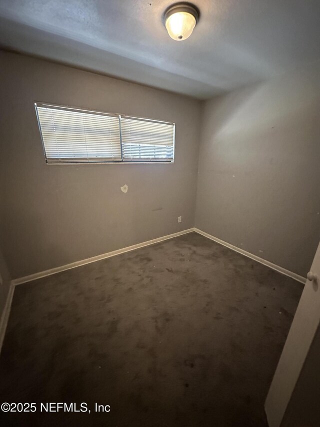 unfurnished room with baseboards and dark carpet