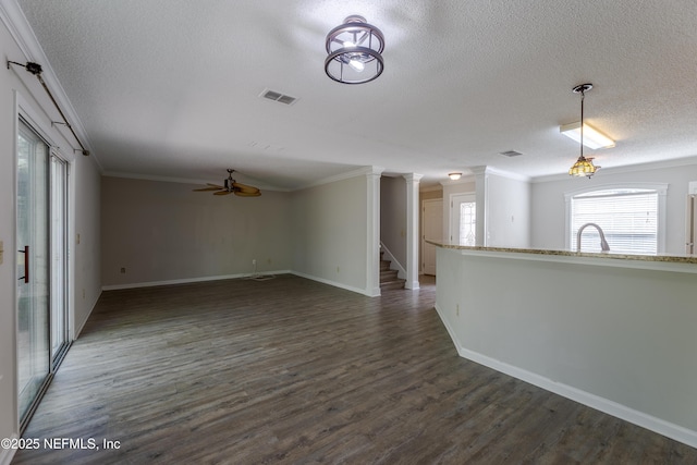 unfurnished living room with visible vents, a ceiling fan, a textured ceiling, dark wood finished floors, and crown molding