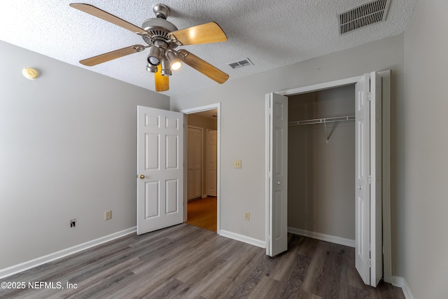 unfurnished bedroom featuring visible vents, a textured ceiling, baseboards, and wood finished floors