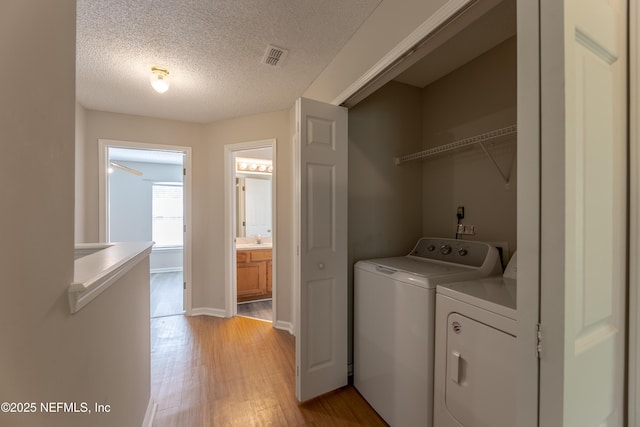 laundry area with visible vents, laundry area, a textured ceiling, light wood-type flooring, and washer and clothes dryer