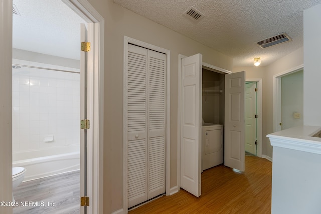 corridor with washer / clothes dryer, visible vents, and light wood-type flooring