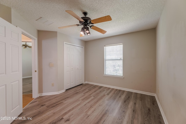 unfurnished bedroom with light wood-style flooring, baseboards, a closet, and a textured ceiling