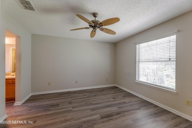 spare room with dark wood-type flooring, a ceiling fan, visible vents, and baseboards