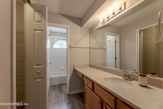 full bathroom featuring baseboards, vanity, a bathtub, wood finished floors, and a textured ceiling