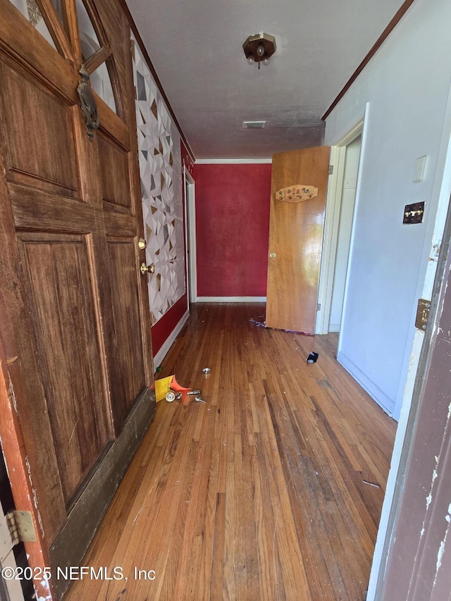 hallway featuring baseboards, visible vents, wood-type flooring, and ornamental molding