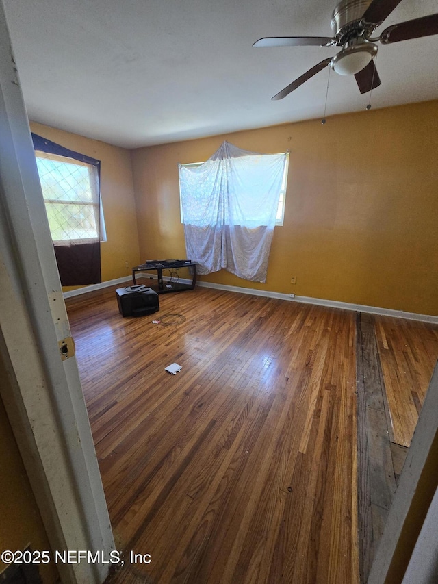 unfurnished room featuring hardwood / wood-style floors, a ceiling fan, and baseboards