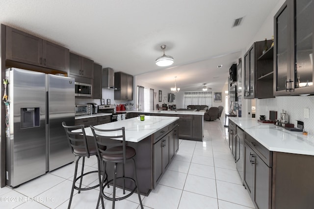 kitchen featuring a peninsula, light tile patterned flooring, decorative backsplash, appliances with stainless steel finishes, and wall chimney range hood