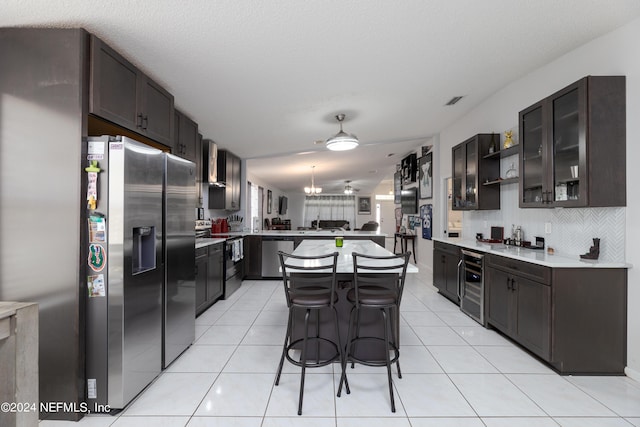 kitchen featuring light tile patterned floors, a peninsula, stainless steel appliances, and wall chimney exhaust hood