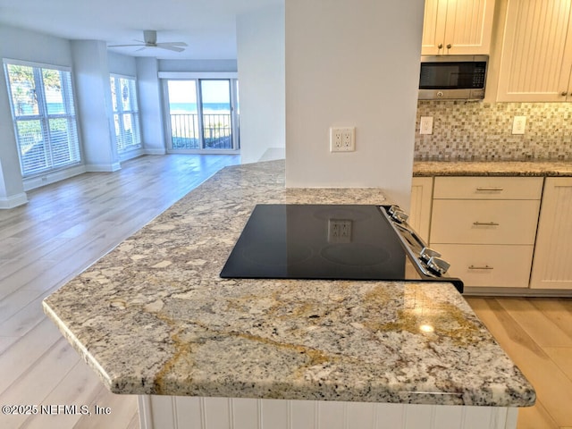 kitchen with tasteful backsplash, stainless steel microwave, a healthy amount of sunlight, and light wood-style floors