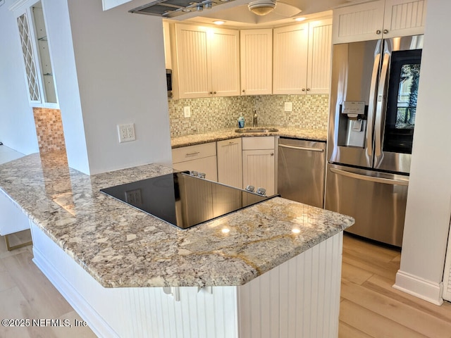 kitchen with a sink, stainless steel appliances, a peninsula, and decorative backsplash