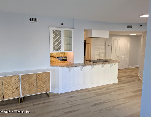 kitchen featuring light wood finished floors, visible vents, black electric stovetop, and light stone countertops