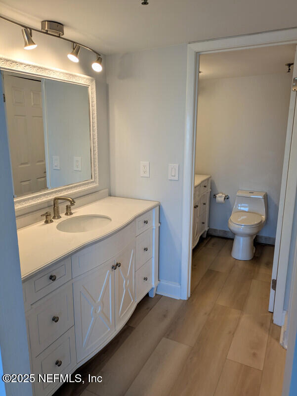 bathroom with toilet, vanity, baseboards, and wood finished floors