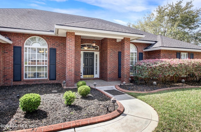 property entrance featuring brick siding and a shingled roof