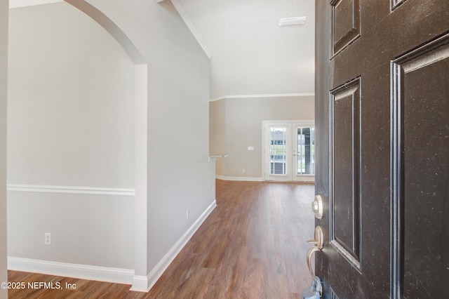 hall with arched walkways, crown molding, baseboards, and wood finished floors