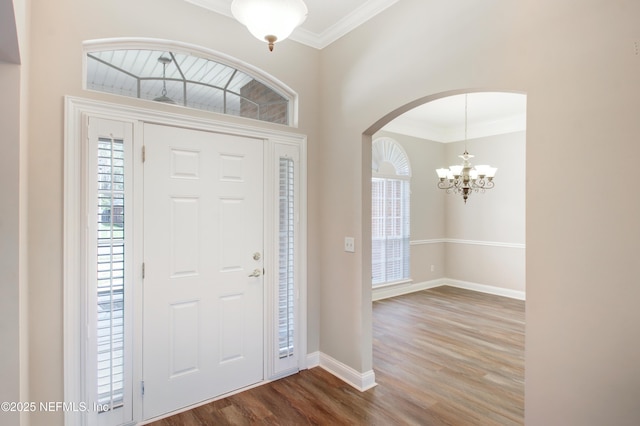 foyer with wood finished floors, arched walkways, an inviting chandelier, crown molding, and baseboards