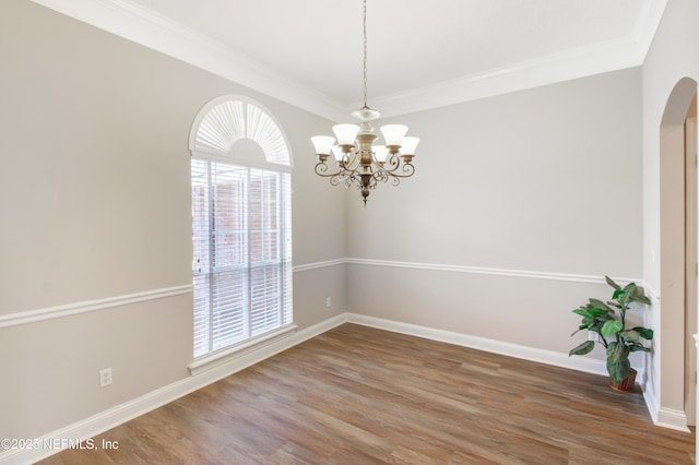 empty room featuring crown molding, baseboards, an inviting chandelier, wood finished floors, and arched walkways