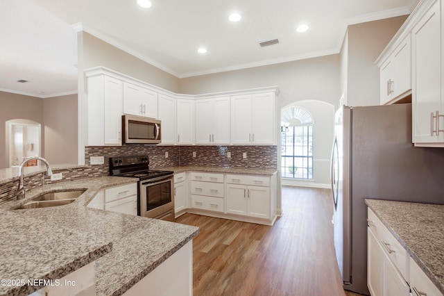 kitchen featuring arched walkways, ornamental molding, decorative backsplash, a sink, and appliances with stainless steel finishes