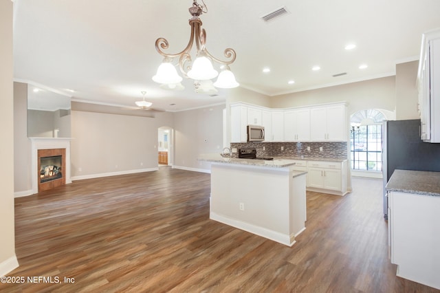 kitchen featuring stainless steel microwave, backsplash, arched walkways, an inviting chandelier, and white cabinets