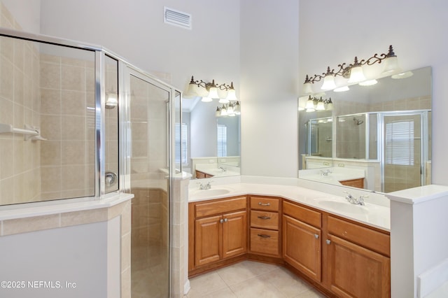 full bath featuring tile patterned flooring, visible vents, double vanity, a stall shower, and a sink