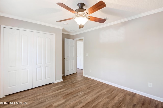 unfurnished bedroom featuring ceiling fan, baseboards, ornamental molding, wood finished floors, and a closet