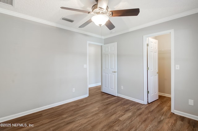 unfurnished bedroom featuring visible vents, crown molding, a walk in closet, and wood finished floors