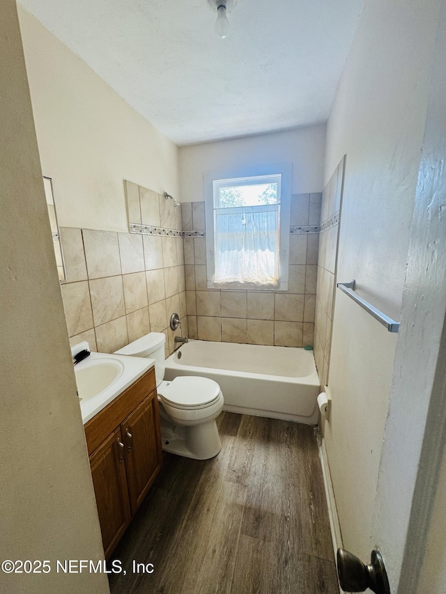 full bath with toilet, wood finished floors, tile walls, a bath, and vanity