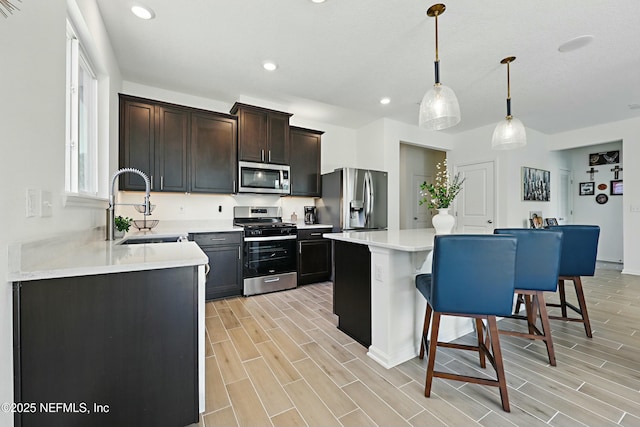 kitchen with a kitchen breakfast bar, wood finish floors, appliances with stainless steel finishes, and a sink