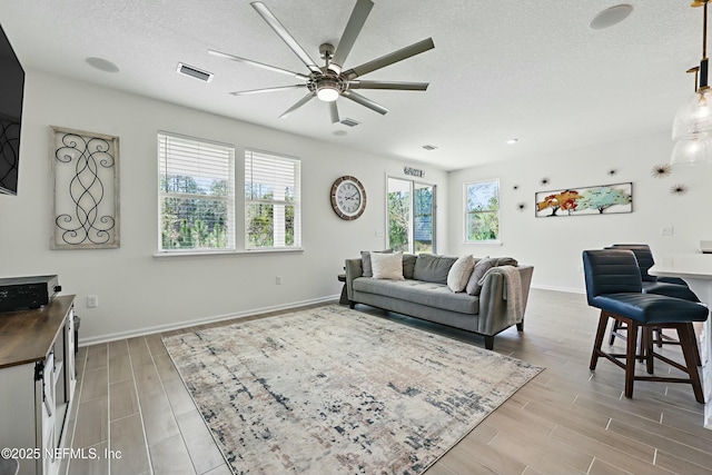 living area with baseboards, visible vents, wood finish floors, ceiling fan, and a textured ceiling