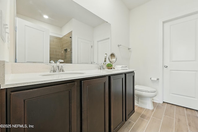 full bath featuring double vanity, tiled shower, toilet, and a sink