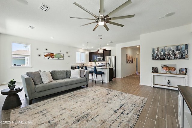 living area with wood finish floors, a ceiling fan, visible vents, and a healthy amount of sunlight