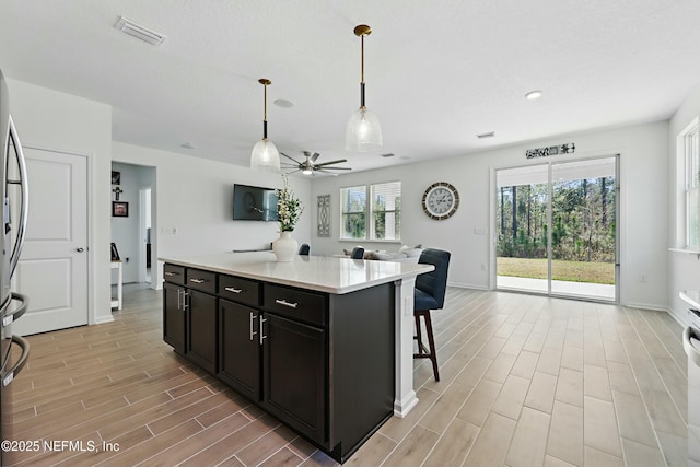 kitchen featuring visible vents, wood finish floors, decorative light fixtures, open floor plan, and a ceiling fan