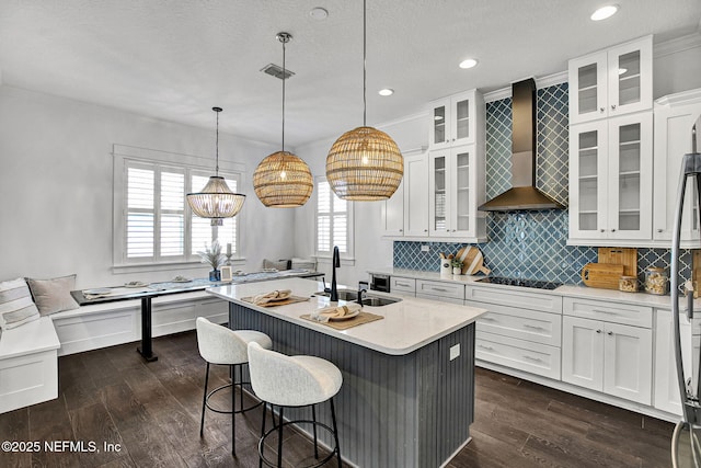 kitchen with dark wood finished floors, black electric stovetop, a sink, light countertops, and wall chimney range hood