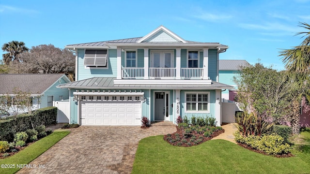 traditional-style house featuring a balcony, fence, a standing seam roof, decorative driveway, and metal roof