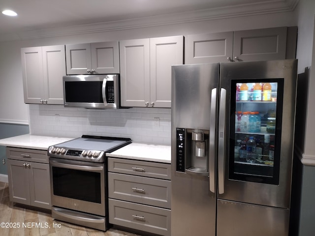 kitchen featuring decorative backsplash, gray cabinetry, stainless steel appliances, and crown molding