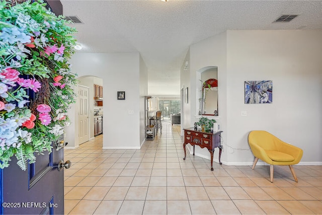 foyer entrance with light tile patterned floors, visible vents, arched walkways, and a textured ceiling