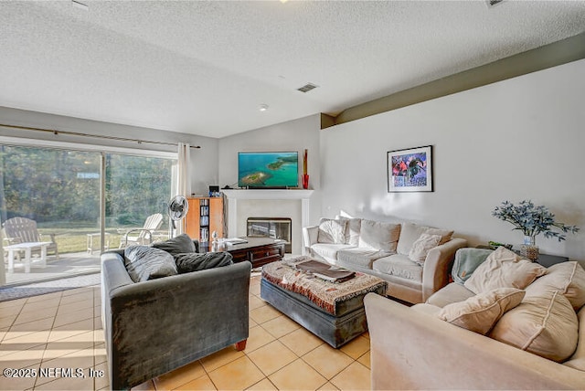 living area with visible vents, a textured ceiling, a glass covered fireplace, light tile patterned floors, and lofted ceiling