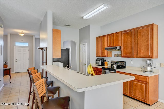 kitchen featuring a kitchen bar, under cabinet range hood, refrigerator, arched walkways, and stainless steel electric range oven