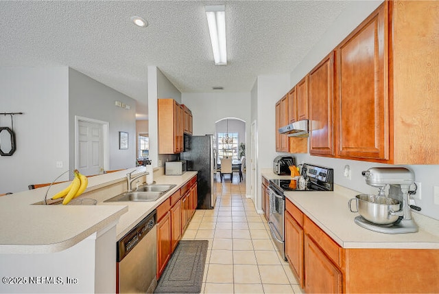 kitchen featuring under cabinet range hood, a sink, stainless steel appliances, a peninsula, and light tile patterned floors