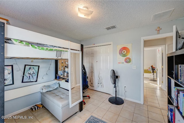 bedroom featuring light tile patterned floors, visible vents, a textured ceiling, and a closet