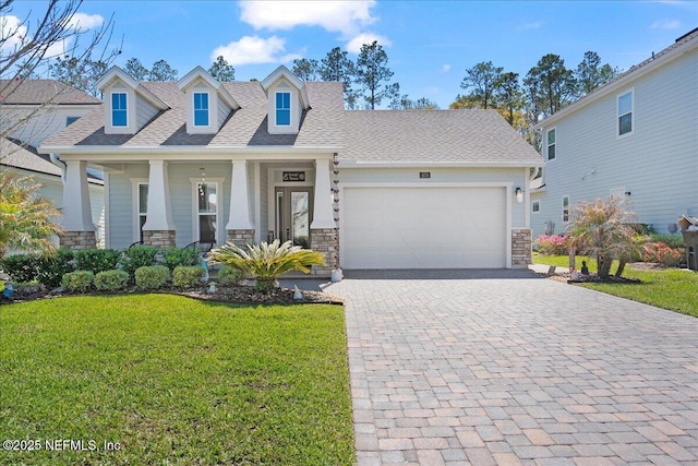 view of front of property featuring a shingled roof, a front yard, decorative driveway, a garage, and stone siding