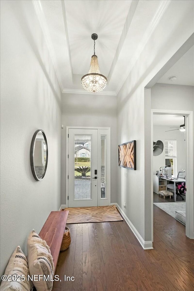 foyer entrance featuring hardwood / wood-style floors, baseboards, a tray ceiling, crown molding, and a chandelier