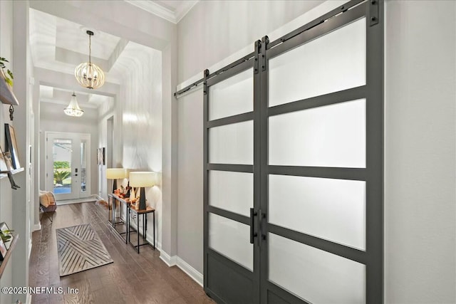 foyer entrance featuring dark wood finished floors, a barn door, crown molding, baseboards, and a chandelier