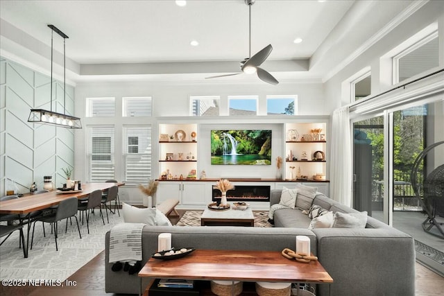 living room with light wood finished floors, a lit fireplace, a high ceiling, and a ceiling fan