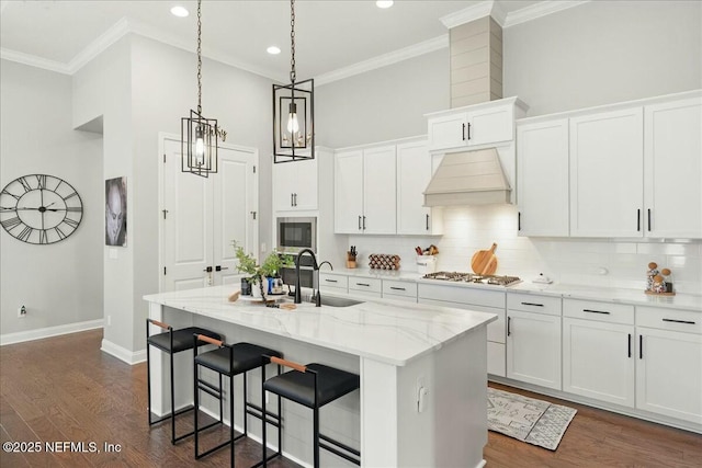 kitchen featuring a center island with sink, a sink, tasteful backsplash, stainless steel appliances, and custom exhaust hood