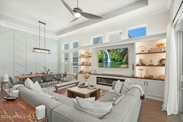 living room with dark wood-style floors, ceiling fan with notable chandelier, built in shelves, and a tray ceiling