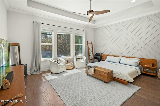 bedroom with crown molding, an accent wall, a raised ceiling, and wood finished floors