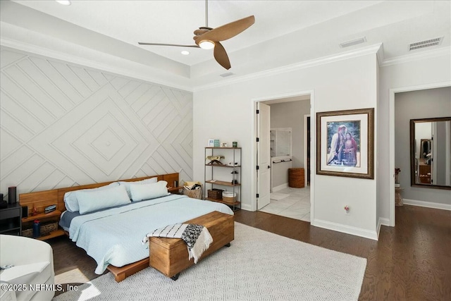 bedroom featuring visible vents, wood finished floors, crown molding, baseboards, and an accent wall