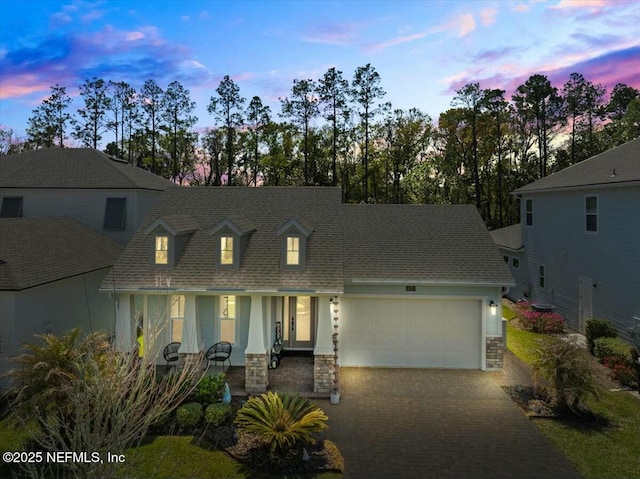 view of front facade featuring stone siding, a shingled roof, decorative driveway, and a garage