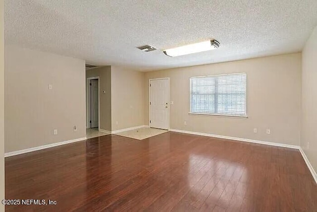 empty room with visible vents, a textured ceiling, baseboards, and wood finished floors