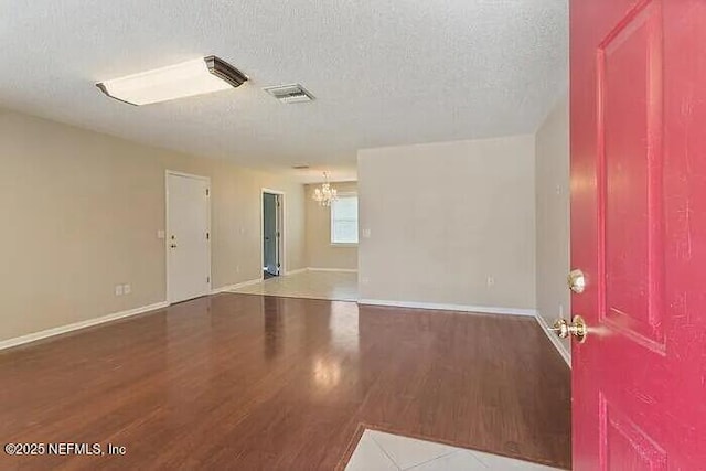 unfurnished room with visible vents, a textured ceiling, wood finished floors, an inviting chandelier, and baseboards